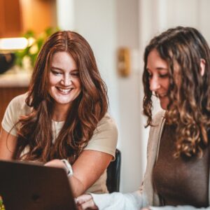 Jen and Abigail sitting at table and looking at laptop smiling